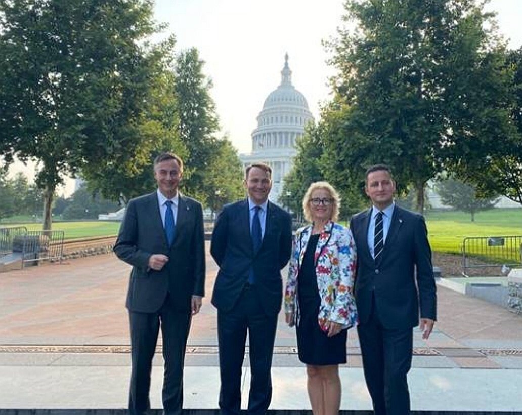 A group of people posing for a photo in front of a white buildingDescription automatically generated