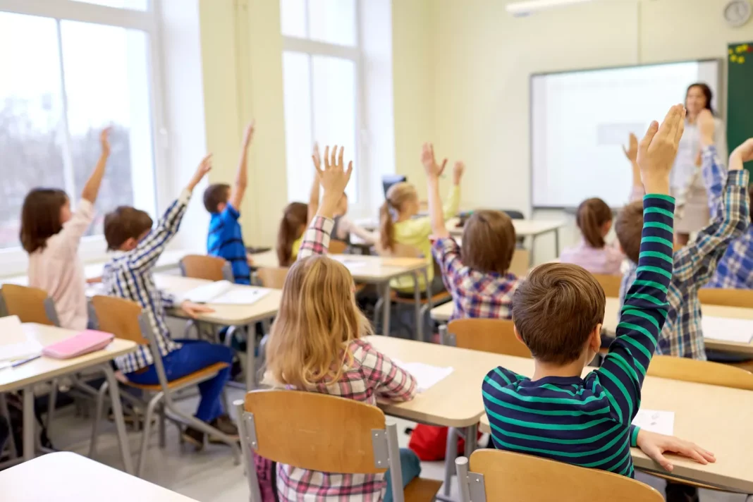 group-of-school-kids-raising-hands-in-classroom-860597978-5ab59c403418c600365665f3