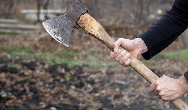 A man holds an ax in his hands against on black background.