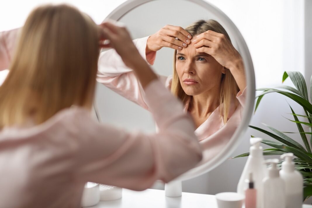 Stressed,Mature,Lady,With,Pimple,On,Forehead,Looking,In,Mirror