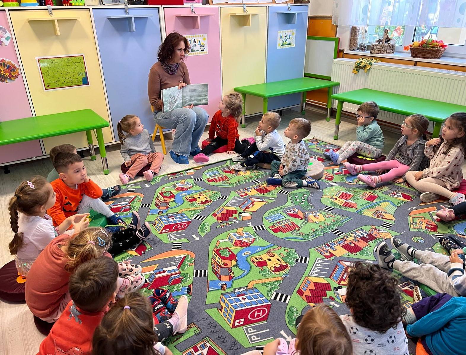 Copii fericiți așezați în cerc, ascultând cu atenție o poveste citită cu voce tare.