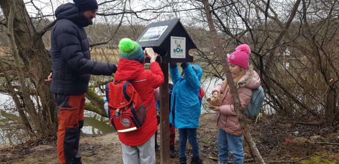 Persoană observând păsări ce iernează cu un binoclu, pe fundalul Muzeului ASTRA