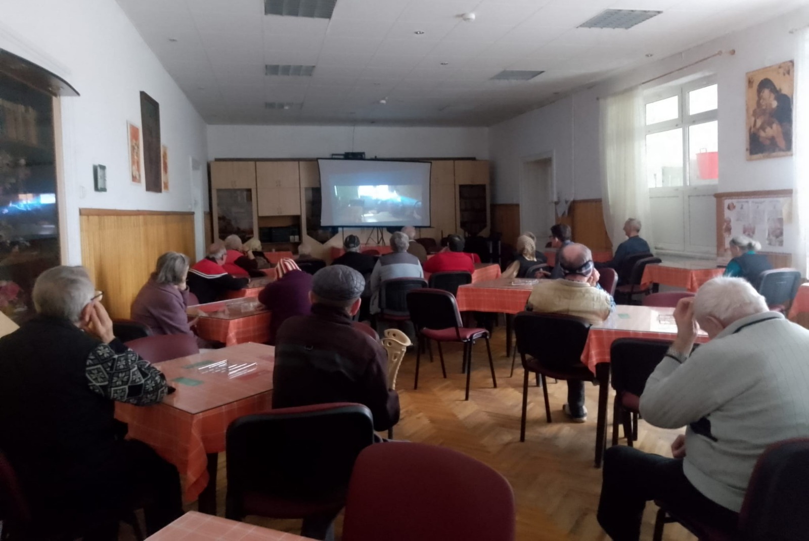 Seniori privind un film la o proiecție organizată de serviciile mobile ale Bibliotecii ASTRA.