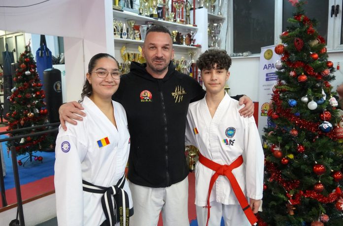 Tineri campioni la taekwon-do, copii de preot, pozând alături de trofee și diploma de premianți