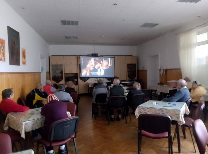 Seniori participând la o activitate de socializare și vizionare de film într-un grup