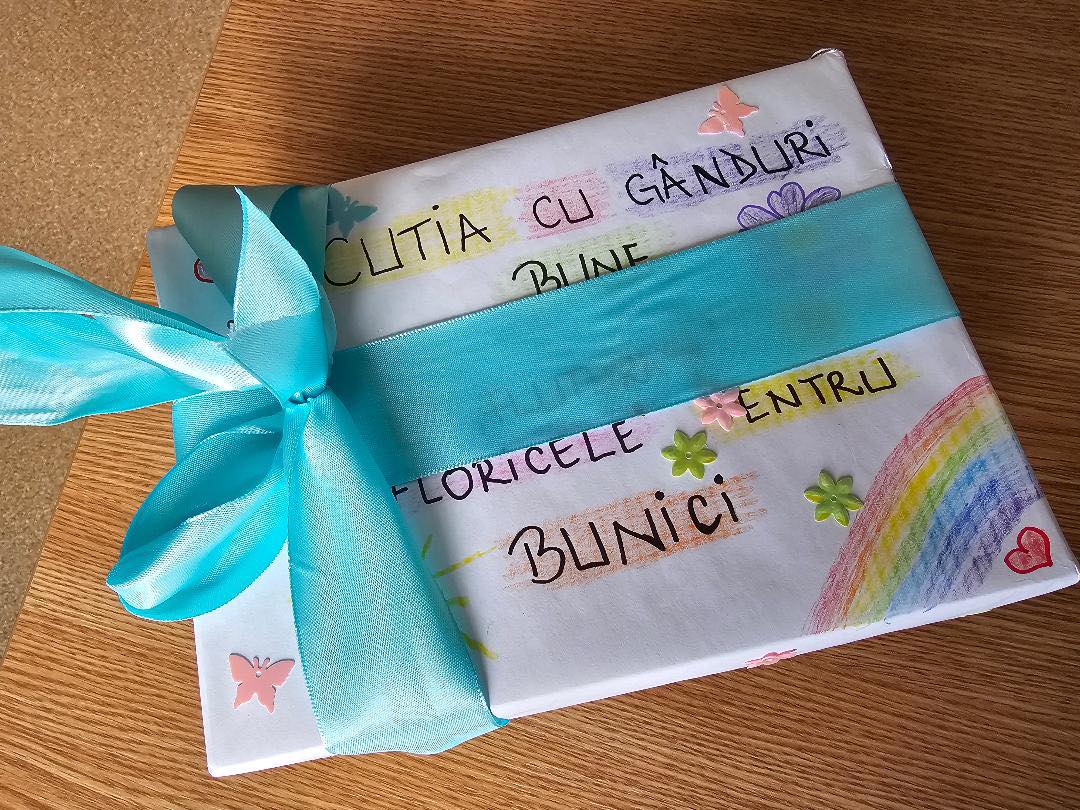 Copii și bunicii scot gânduri bune din Cutia gândurilor bune, cu zâmbete pe fețe.