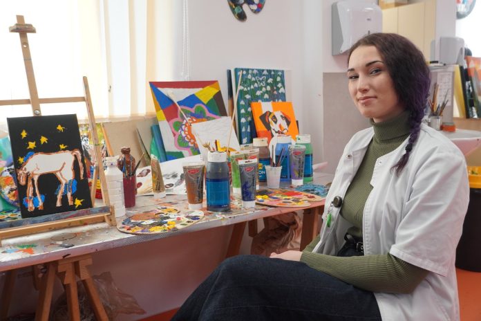 Portret al Andreei, artistă care pictează și scuipă flăcări, privind cu determinare.